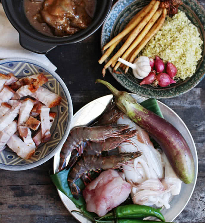 Bún mắm được biết là chúng có nguồn gốc từ nước bạn Campuchia. Quá trình du nhập vào Việt Nam được cải biên sau cho phù hợp với khẩu vị của người dân ta. Thường được nấu bằng mắm cá linh hoặc cá sặc hoặc có nhiều nơi trộn cả hai thứ cá đấy vào nấu để tăng hương vị. Chúng mang hương vị đậm đà hơn bún nước lèo, bún mắm chúng được ăn chung với heo quay, chả cá, cá lóc, mực, tôm, huyết,.. ăn kèm với rau sống.  Còn đối với miền Tây - đặc biệt ở hai tỉnh Trà Vinh và Sóc Trăng, thường nấu bằng mắm bù hốc và người ta gọi là bún nước lèo, chúng được ăn chung với cá lóc, huyết, rau sống (rau muống chẻ, cọng bông súng, rau đắng, bắp chuối, kèo nèo, giá và rau diếp cá ), giấm ớt,... đơn giản rất nhiều.  Khoảng những năm 1970, bún mắm được đưa lên Sài Gòn và được nhiều người yêu thích ngay lập tức do mang đầy hương vị của đồng nội, miền quê với cách nêm ngon đậm đà và dân dã. Món ăn khó cưỡng lại cho đến ngày nay và tùy vào nơi khác nhau ta có cách nấu ăn khác nhau để phù hợp với nơi đó. Dù nấu như thế nào thì bún mắm vẫn được coi là món ăn không thể quên sau khi ta thưởng thức lần đầu.  Nguyên liệu làm Bún mắm: Chả cá thác lác: 200 gr Mắm cá sặc: 300 gr (hoặc mắm cá linh). Đối với một số gia đình, người ta thường dùng cả 2 loại mắm vào nấu chung để tăng hương vị đậm đà cho món bún mắm. Heo quay: 200 gr Cá diêu hồng: 1 con (800gr). Ta có thể thay thế bất kì loại cá nào mà ta thích ăn Mực: 300 gr Tôm: 400 gr Ớt: 3 trái Hẹ: 20 gr Cà tím: 2 trái Ớt sừng: 5 trái Thơm: 1/2 trái Hành tím: 2 củ Ngải bún: 50gr Hành lá: 3 nhánh Trái dừa: 1-2 trái Sả: 3 tép Rau ăn kèm 1 ít (giá/ rau đắng/ bông súng/ cù nèo/ hoa chuối) Bún tươi: 500gr Nước mắm: 1/2 muỗng cà phê Dầu ăn: 7 muỗng canh Gia vị thông dụng 1 ít (muối/ hạt nêm/ tiêu xay/ đường/ bột ngọt) Cách chọn mua nguyên liệu tươi ngon cho món bún mắm: Cách chọn mua mắm cá ngon, chất lượng:  - Bạn nên chọn mua những loại mắm được đóng hộp sẵn để đảm bảo an toàn vệ sinh thực phẩm. Bạn có thể mua mắm ngoài chợ nếu bạn đã ở quen với nó.  - Ưu tiên chọn những loại có thương hiệu uy tín, thông tin xuất xứ, nguyên liệu sản xuất rõ ràng. Không chọn những loại khi ngửi có mùi hôi khó chịu hoặc bề mặt nổi váng mỡ bất thường.  Cách chọn mua mực tươi ngon:  - Bạn nên chọn những con có phần da màu tím sẫm, còn phần thân có màu trắng sữa.  - Có thể kiểm tra độ tươi ngon của mực bằng cách dùng tay nhấn thử, nếu cảm nhận được độ đàn hồi tốt thì nên mua nhé. Không chọn những con mực khi sờ quá mềm, khi ngửi có mùi hôi và bề mặt có nhiều lốm đốm đen bất thường.  Cách chọn mua tôm tươi ngon:  - Những con tôm tươi thường có phần vỏ trong suốt, khi ngửi cảm nhận được mùi thơm nước biển đặc trưng. Như thế tôm đấy khi ăn ta sẽ cảm nhận được độ tươi và ngon của nó.  - Ưu tiên chọn con có phần đầu và thân tôm dính chắc vào nhau và phần chân tôm xếp đều hướng vào trong. Không chọn mua những con có phần vỏ quá mềm, khi sờ bị nhớt và ngửi có mùi hôi.  Cách chọn mua thịt heo tươi ngon:  - Những miếng thịt ngon thường có phần nạc màu đỏ hồng, còn phần mỡ thì màu trắng đục bắt mắt. Ta có thể chọn bất cứ phần thịt nào mà ta thích ăn như đùi, ba rọi, thịt nạc,....  - Bên cạnh đó, bạn nên chọn những miếng có tỉ lệ nạc với mỡ cân bằng nhau thì khi ăn sẽ ngon hơn nhé.  - Không chọn những miếng bề mặt đã bị chảy nhớt, phần thịt không còn tươi và khi ngửi có mùi hôi khó chịu. Các miếng thịt ấy có nhiều vi khuẩn gây đau bụng khi ta ăn chúng.  Cách chọn mua cá diêu hồng/cá lóc tươi ngon:  - Bạn chọn những con cá diêu hồng/cá lóc có phần vảy dính chặt vào thân cá và có vẻ ngoài sáng óng ánh.  - Những con cá tươi thường có phần mắt trong, hơi lồi, không chọn những con có phần mắt chảy nhớt hoặc đục ngầu.  - Không chọn những con khi sờ không cảm nhận được độ đàn hồi của phần thịt cũng hơi khi ngửi có mùi hôi. Những con ấy sắp chết, họ sẽ bỏ hoặc bán rẻ lại cho bạn nhưng khi ăn sẽ có mùi khó chịu và không ngon.  Bún mắm được chế biến như thế nào? Sơ chế các nguyên liệu: Sả lặt bỏ phần lá úa và gốc rễ, rửa sạch, lấy 1 tép sả ra băm nhuyễn. Phần còn lại ta đập sơ, ta bẻ đôi tép sả và lấy phần lá mỏng quấn chặt thay phần dây. Hành tím lột bỏ vỏ, rửa sạch, một củ thì bạn cắt làm đôi, còn củ còn lại thì băm nhuyễn. Ngải bún rửa sạch, dùng dao đập dập. Ngải bún được coi là thành phần khó có thể thiếu vì chúng là tăng hương vị cho bún mắm đặc trưng hơn. Hành lá cắt bỏ lá úa vàng và rễ, rửa sạch, cắt phần đầu hành để riêng, còn lá hành thì cắt nhỏ. Ớt sừng rửa sạch, dùng dao rạch đôi theo chiều dọc rồi cẩn thận móc bỏ phần hạt ớt đi dùng chúng làm chả cá chiên. Còn ớt trái thì rửa sạch rồi băm nhuyễn. Thơm bạn gọt bỏ phần vỏ và mắt thơm, rửa sạch rồi cắt khúc. Cà tím rửa sạch rồi cắt khúc vừa ăn. Cá diêu hồng hay cá lóc bạn rửa sạch sạch, loại vỏ phần ruột cá bên trong, phần vẩy với vây cá. Sau đó bạn cắt cá làm 3 khúc, khúc đầu, khúc đuôi bạn cất để thực hiện món ăn khác, với món bún mắm, bạn chỉ dùng khúc giữa thôi nhé! Tiếp tục dùng dao tách bỏ phần xương cá rồi rửa thật sạch với nước. Cắt cá thành từng khúc vừa ăn. Còn với mực thì bạn lột bỏ phần da rồi rửa thật sạch lại với nước. Heo quay thì bạn cắt thành miếng vừa ăn, dày khoảng 1/2 lóng tay. Nấu mắm cá:  - Bắc nồi lên bếp, cho vào khoảng 500ml nước. Sau đó, cho 300gr mắm cá sặc/cá linh vào trong nước, đợi nước sôi cho cá mềm, dùng muỗng dằm nhuyễn phần xác cá và nấu đến khi phần xác cá rục. Ta lấy vợt lược bỏ phần xương cá bỏ đi, cần lược qua 2-3 lần để lọc sạch xương. Tránh mắc cổ khi ăn.  - Để mắm cá thơm hơn, bạn cho thêm 1 tép sả, 1 củ hành tím vào trong nước dùng nhá.  Làm chả ớt:  - Cho hành lá vào chén đựng chả cá và trộn đều để hành hòa quyện vào chả cá. Tiếp đến, cho tất cả chả cá vào một túi kính, nêm vào 1 muỗng cà phê hạt nêm, 1/3 muỗng cà phê bột ngọt, 1/2 muỗng cà phê đường, 1/2 muỗng cà phê tiêu và 1 muỗng cà phê dầu ăn.  - Sau đó, dùng tay nhào thật kỹ phần chả cá để gia vị thấm đều. Cuối cùng, nêm thêm 1/2 muỗng cà phê nước mắm rồi trộn đều lần nữa.  - Dùng muỗng múc chả cá nhồi vào từng quả ớt đã chuẩn bị. Tương tự, bạn làm đến hết phần chả cá và ớt đã chuẩn bị.  - Sau khi đã nhồi xong, bạn bắc một cái chảo lên bếp, cho vào khoảng 3 muỗng canh dầu ăn, đợi dầu nóng thì gắp phần chả ớt vào và chiên vàng đều 2 mặt thì gắp ra đĩa để ráo dầu.  Luộc tôm, mực, cá:  - Bắc một nồi nước lên bếp, cho vào 1/2 muỗng cà phê muối, 1/3 muỗng cà phê bột ngọt và đun sôi. Khi nước sôi thì bạn cho mực vào luộc khoảng 2 phút.  - Mực chín thì bạn cho tiếp tôm vào luộc trong khoảng 5 phút nữa. Sau 5 phút, tôm và mực đều chín rồi thì bạn vớt ra tô cho ráo nước.  - Cuối cùng, cho cá diêu hồng vào luộc khoảng 4 phút, rồi cẩn thận vớt cá ra. Ta có thể thay thế bất kể cá gì mà gia đình thường ăn và hợp khẩu vị.  Nấu nước dùng cho bún mắm:  - Bắc nồi lên bếp, cho vào nồi khoảng 2 lít nước. Sau 30 phút nấu mắm cá thì phần cá đã rục mềm, bạn đổ mắm cá qua rây để loại bỏ phần xác cá, phần mắm cá đã lọc thì cho vào nấu nước dùng, cho tất cả thơm đã cắt khúc vào, đun khoảng 1 giờ.  - Tiếp đến, đổ phần nước lúc nãy dùng để luộc tôm, mực, cá qua rây vào. Nước luộc tôm, mực sẽ làm tăng độ ngọt cho nước dùng hoặc có thể ta sử dụng nước dừa tươi, dừa khô.  - Bắc một cái chảo lên bếp, cho vào khoảng 3 muỗng canh dầu ăn, đợi dầu sôi thì cho phần sả đã băm nhỏ vào xào khoảng 1 phút thì cho tiếp ớt đã băm nhuyễn vào, ngải bún xào thêm 3 phút nữa thì cho hỗn hợp này vào nồi nước dùng.  - Nêm vào 1 muỗng canh đường, 1 muỗng canh hạt nêm và 1/2 muỗng cà phê bột ngọt. Cho tất cả phần cà tím vào, đun thêm khoảng 10 phút nữa, nêm nếm lần cuối cho hợp khẩu vị bạn rồi tắt bếp, thêm một xíu hẹ vào để nước dùng thơm hơn.  Hoàn thành:  - Để hoàn thành món bún mắm này, bạn cho một lượng bún đủ ăn vào tô, xếp các loại topping gồm tôm, mực, cá, múc nước dùng chang vào sắp xỉ với bún hoặc nếu bạn muốn ăn nước nhiều vẫn cho thêm.  - Xếp lên trên một ít thịt heo quay và chả ớt, cho xíu rau đắng lên trên để món ăn thêm hấp dẫn. Trộn đều và thưởng thức nhé!  Bún mắm đạt chuẩn:  - Bún mắm sau khi hoàn thành có phần nước dùng trong veo, đẹp mắt. Nước dùng đậm đà, ngọt thanh, kết hợp vị ngọt của nhiều loại nguyên liệu mang đến cho bạn cảm giác vô cùng tròn vị, ngon miệng.  - Topping tươi ngon, đậm đà, chấm cùng nước me làm dậy mùi ngon hơn. Món ăn chắc chắn sẽ khiến mọi người gia đình bạn thích mê.  Lưu ý khi làm bún mắm thành công:  - Khi nấu mắm để lọc qua rây lấy phần nước cốt bạn không nên cho quá nhiều nước vì như vậy sẽ làm loãng phần nước cốt mắm.  - Để món bún mắm ăn không ngán bạn có thể kết hợp thêm rau đắng, rau muống hay giá.  Đối với mùa dịch này việc ăn uống trở nên khó khăn hơn vì các hàng quá không mở cửa. Chính vì thế, cách tốt nhất để thưởng thức món ăn vừa an toàn vừa hợp vệ sinh ta có thể nấu ăn ngay tại nhà của mình. Vừa đảm bảo được sự dinh dưỡng, vừa đảm bảo được sức khỏe không bị ảnh hưởng bởi dịch bệnh đang căng thẳng ngoài kia.  Chúc các bạn thành công trong quá trình thực hiện nhé!  CÔNG TY TNHH SẢN XUẤT – THƯƠNG MẠI – DỊCH VỤ – AN THÀNH  Địa chỉ: 47/80 Ao Đôi, Khu Phố 10, Phường Bình Trị Đông A, Quận Bình Tân, TP.HCM  Email: anthanhsale01@gmail.com  Điện thoại: 0903103922  Hotline: 0906312325  Website: https://www.packvn.com/ – https://maydonggoi.vip/  Facebook: https://www.facebook.com/maydonggoianthanh  Pinterest: https://www.pinterest.com/donggoianthanh/_saved/  Instagram: https://www.instagram.com/maydonggoianthanh/  Twitter: https://twitter.com/donggoianthanh  Linkedin: https://www.linkedin.com/in/may-dong-goi-bao-bi-an-thanh/  Youtube: Máy đóng gói An Thành – YouTube.